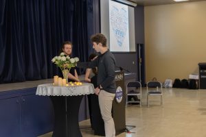 Male college student putting a white rose into a crystal vase that's sitting on a round table