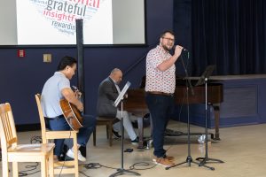 Three men performing a song with one man playing the piano, one man playing the guitar and one man singing.