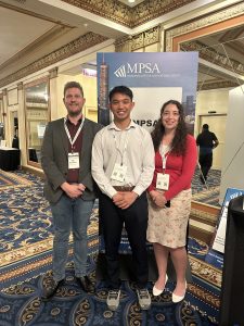 A male professor standing with a male and female college student in a conference room