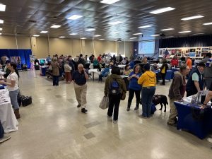 Crowd of people walking through a large room with tables and displays set up