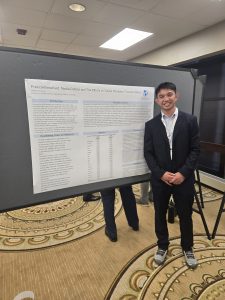 Male college student dressed in a suit standing next to a large poster with data on it on an easel