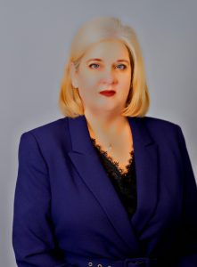 Woman with shoulder-length blonde hair wearing a navy jacket in front of a gray backdrop