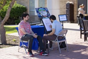 Man seated drawing a caricature of another man who is seated