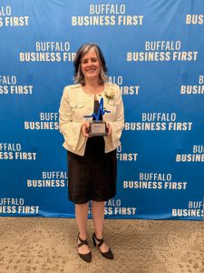 Woman standing in front of a blue backdrop with white text holding a trophy