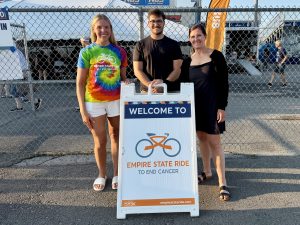 Two women and a man standing behind a sign that says Welcome to Empire State Ride to end cancer