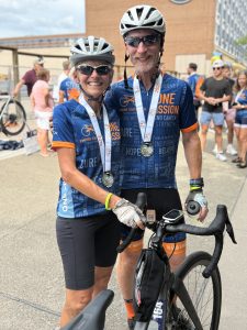 A woman and man wearing cycling apparel and medals around their necks standing together smiling