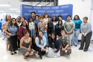 A group of college-aged students standing together in front of a blue Daemen backdrop