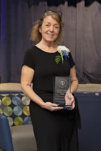 Woman wearing a black dress holding an award standing in front of a stage