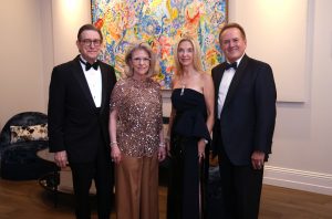 Two men and two women dressed in black tie attire standing together in front of a colorful painting