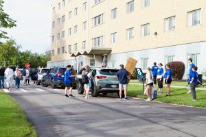 A line of cars in front of Canavan Hall with people unloading students' belongings to take into the residence hall
