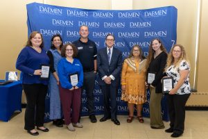 A group of people standing with President Gary A. Olson in front of a blue backdrop with white Daemen University text repeated on it