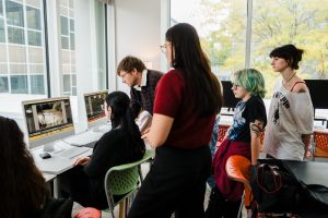 Daemen graphic design professor looks at a computer monitor while students also look on in the classroom