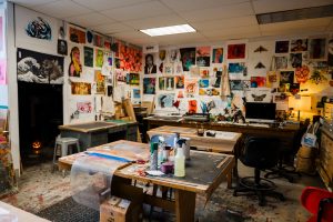 A room filled with artwork on the wall, desks, and art supplies