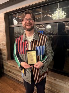 Man dressed in colorful striped button down shirt holding an award plaque