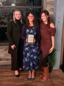Three women standing together holding an award plaque.