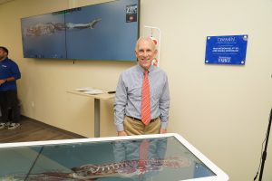 Dr. Fran McDonald stands behind the Anatomage table and next to his donor plaque